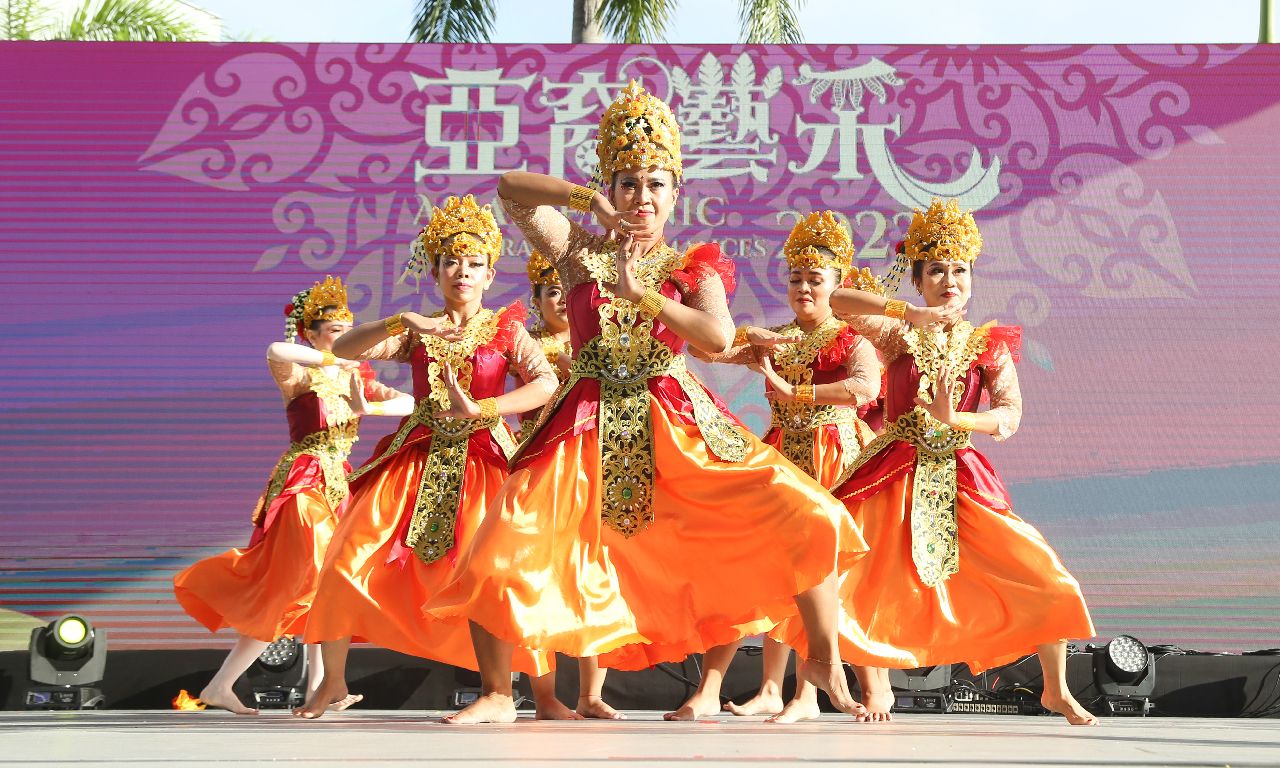 A group of dancers dressed in traditional Southeast Asian costumes perform a cultural dance on stage at the Hong Kong Cultural Centre during the Belt and Road dance festival, showcasing vibrant orange and gold costumes with intricate headpieces.
